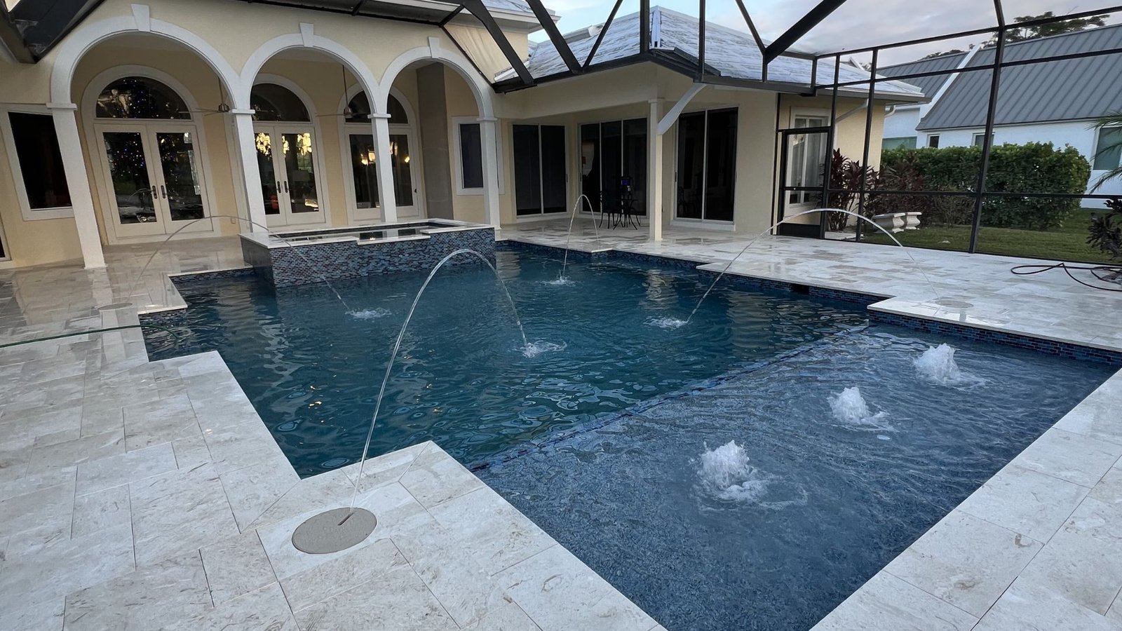 Custom pool with laminar deck jets, bubblers, and raised spa inside a pool cage in Southwest Florida