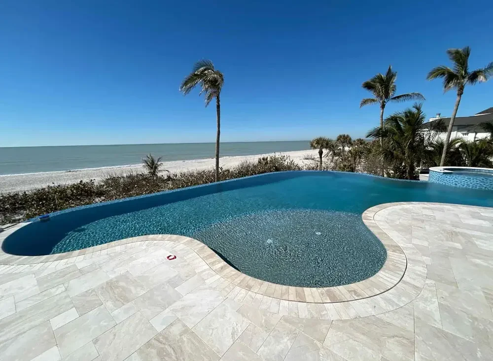 Freeform pool overlooking the beach with palm trees and a travertine deck
